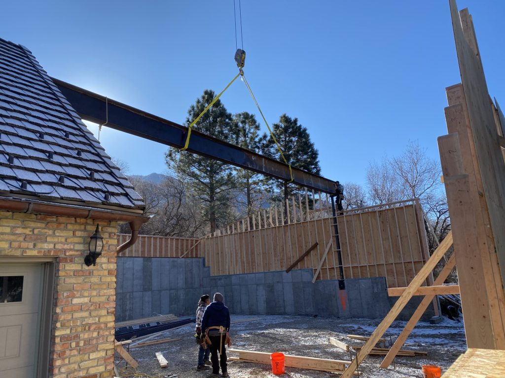 crane lifting a large steel i beam into place on a utah home construction site with workers guiding it into position